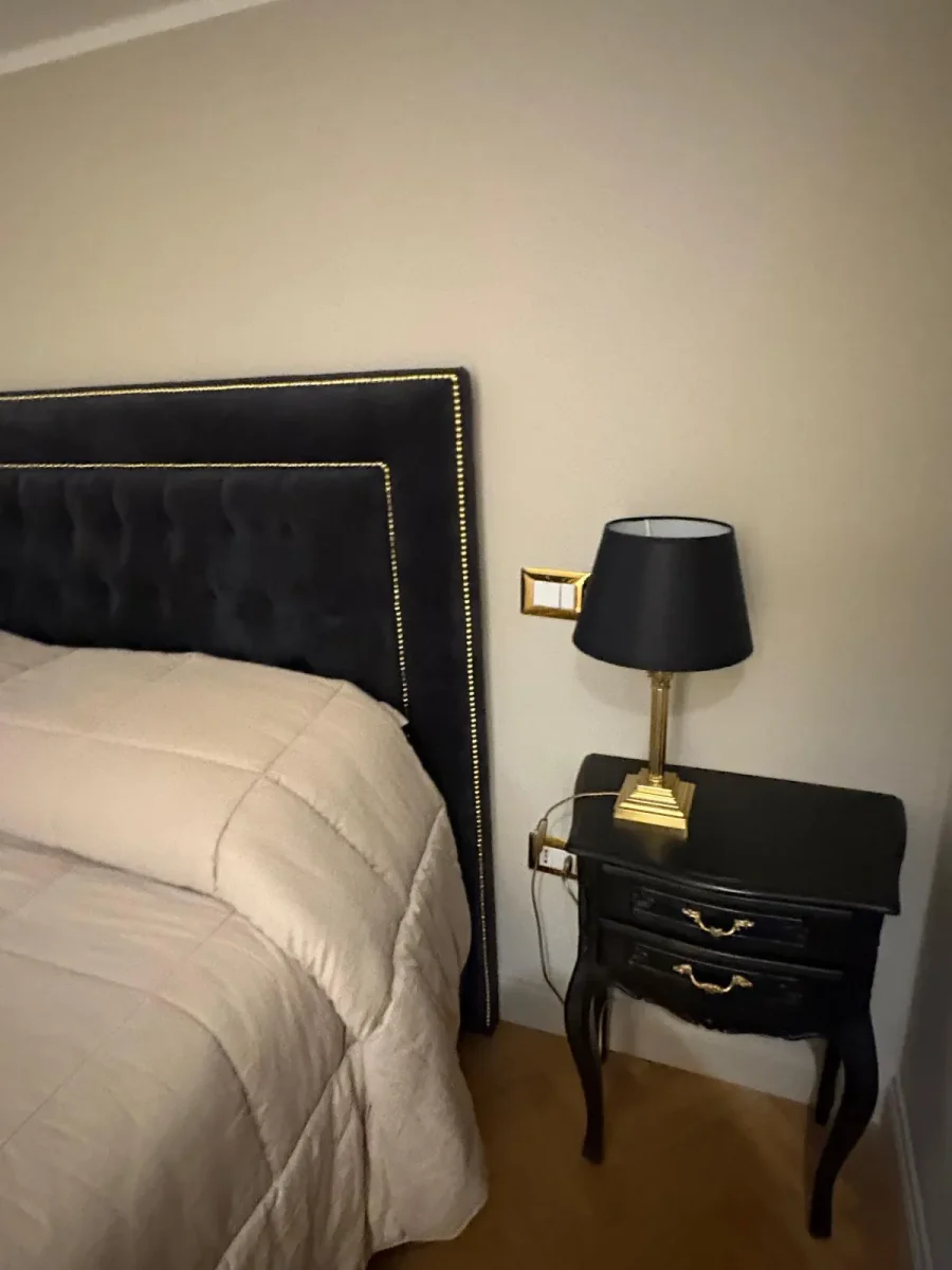 Comodino laccato nero con lampada dal paralume scuro e applique dorata a parete
