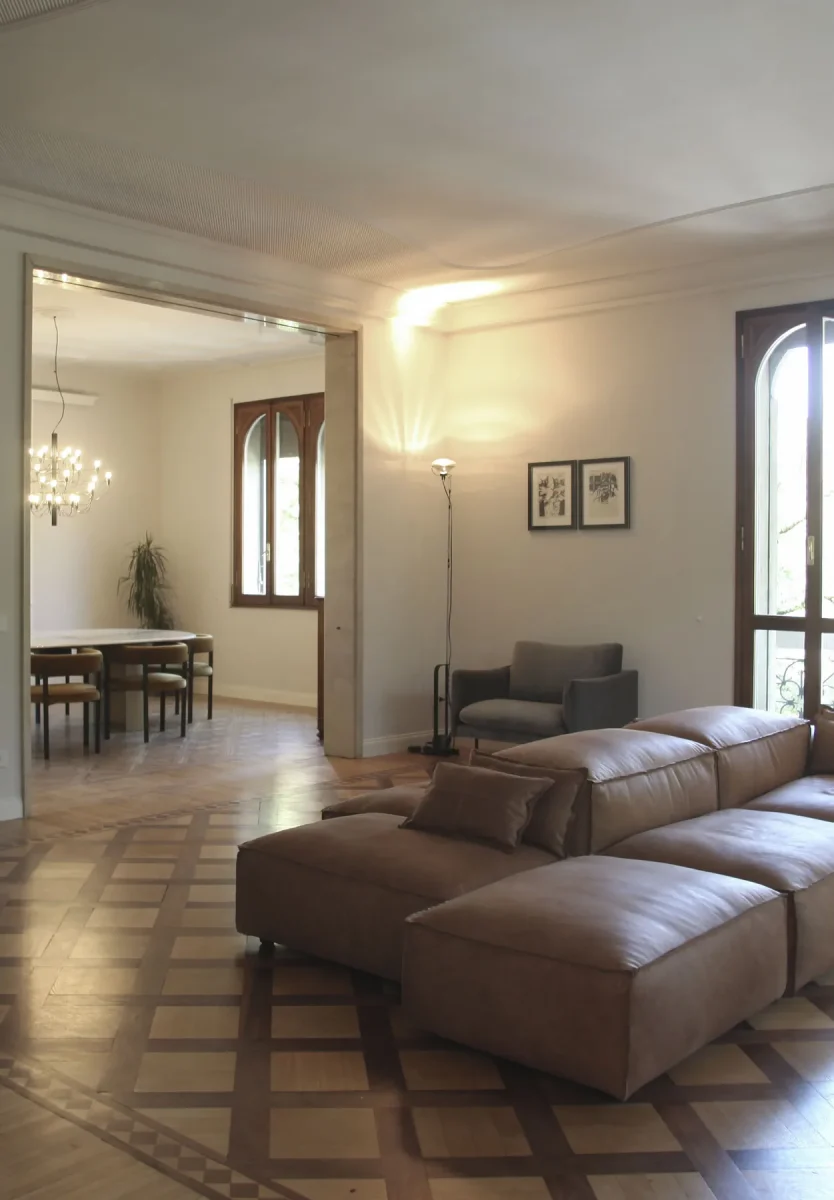 Divano in pelle in primo piano e prospettiva aperta verso la sala da pranzo con lampadario
